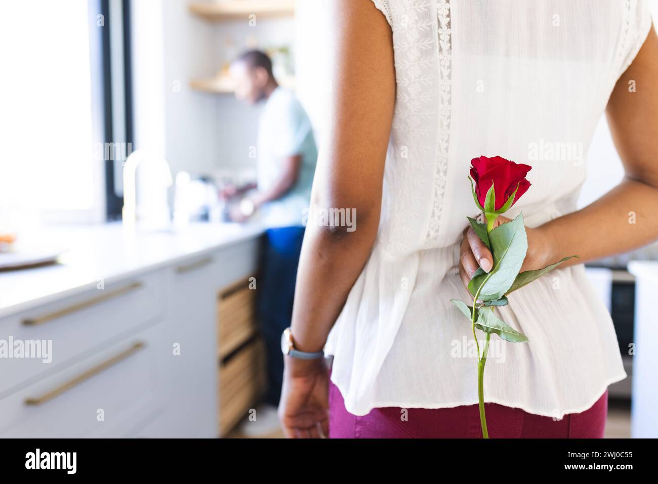 Giovane donna birazziale che tiene una rosa dietro di lei, a casa, con spazio di copia Foto Stock
