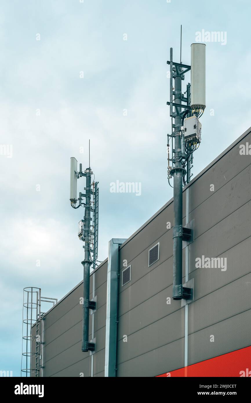 Stazione base di telefonia mobile e antenna del ripetitore di segnale su edifici industriali, vista ad angolo basso Foto Stock