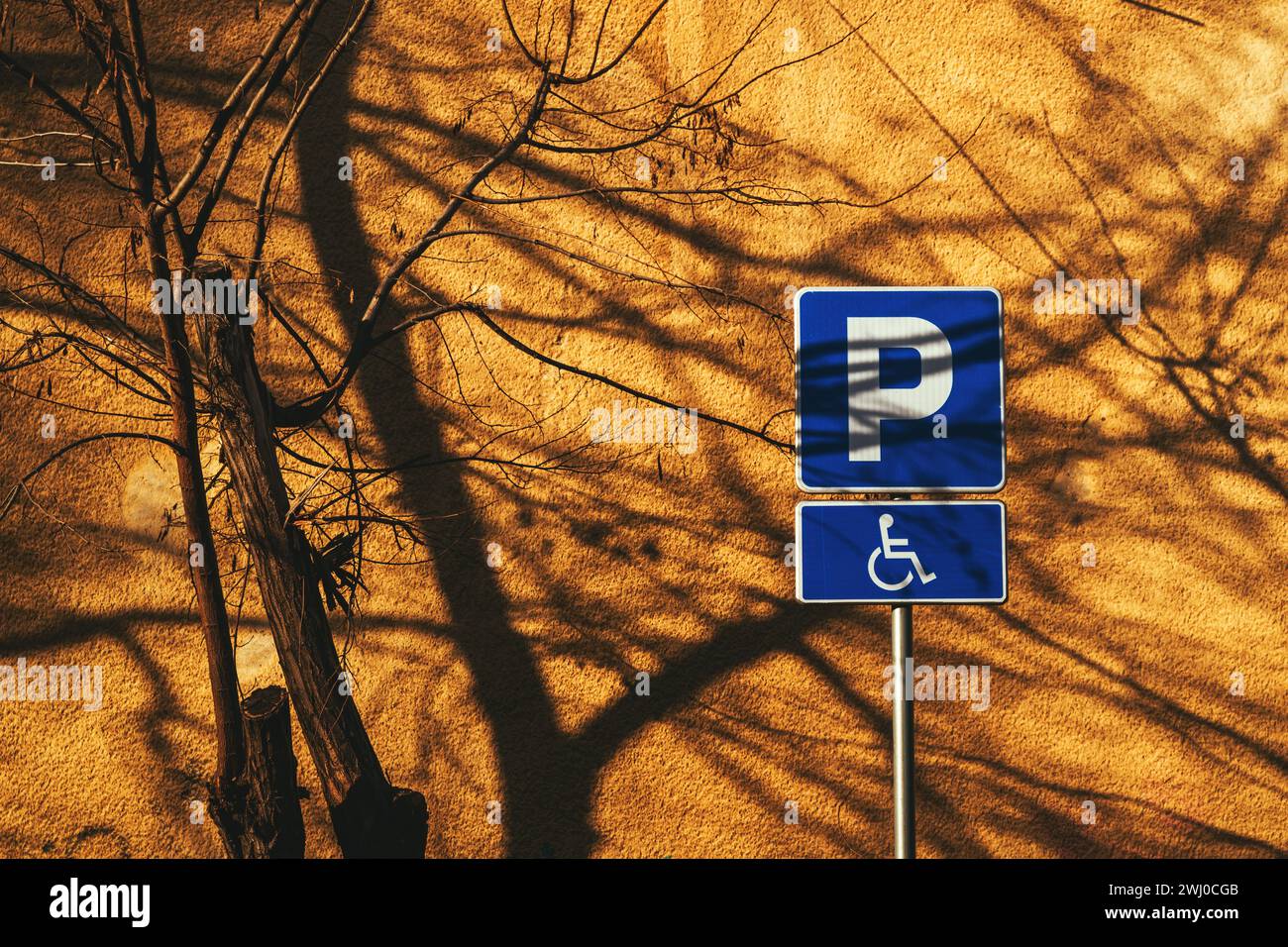 Segnaletica per l'accesso facilitato al parcheggio riservato a persone portatrici di handicap contro le mura gialle Foto Stock