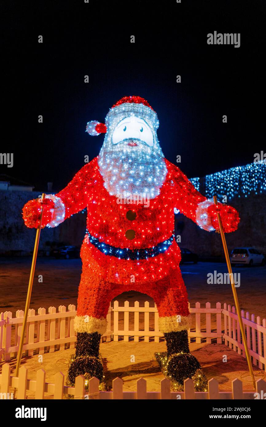 Decorata con ghirlande luminose, la figura di Babbo Natale sugli sci si erge dietro una recinzione bassa Foto Stock