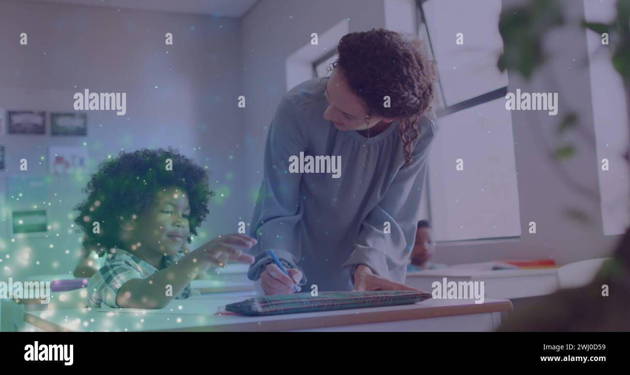 Immagine di particelle di luce su un'insegnante donna felice e diversificata che aiuta il scolaro alla scrivania in classe Foto Stock