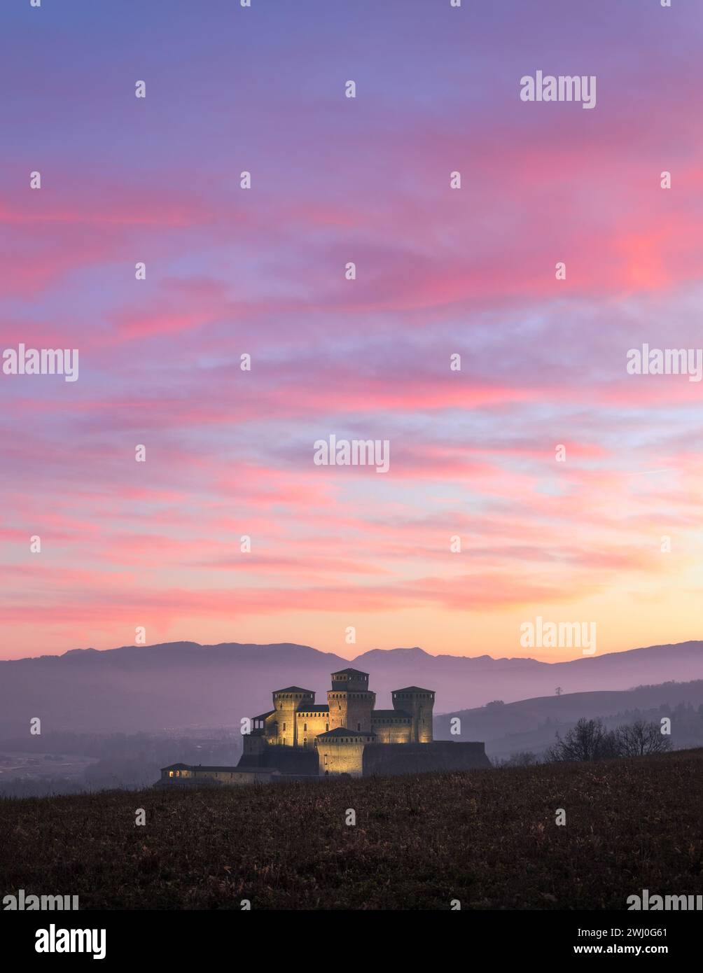 Un maestoso castello emerge dalla collina, bagnato dal soffice bagliore della prima serata invernale. Il cielo è dipinto con sfumature di rosso e arancione, cuoio Foto Stock