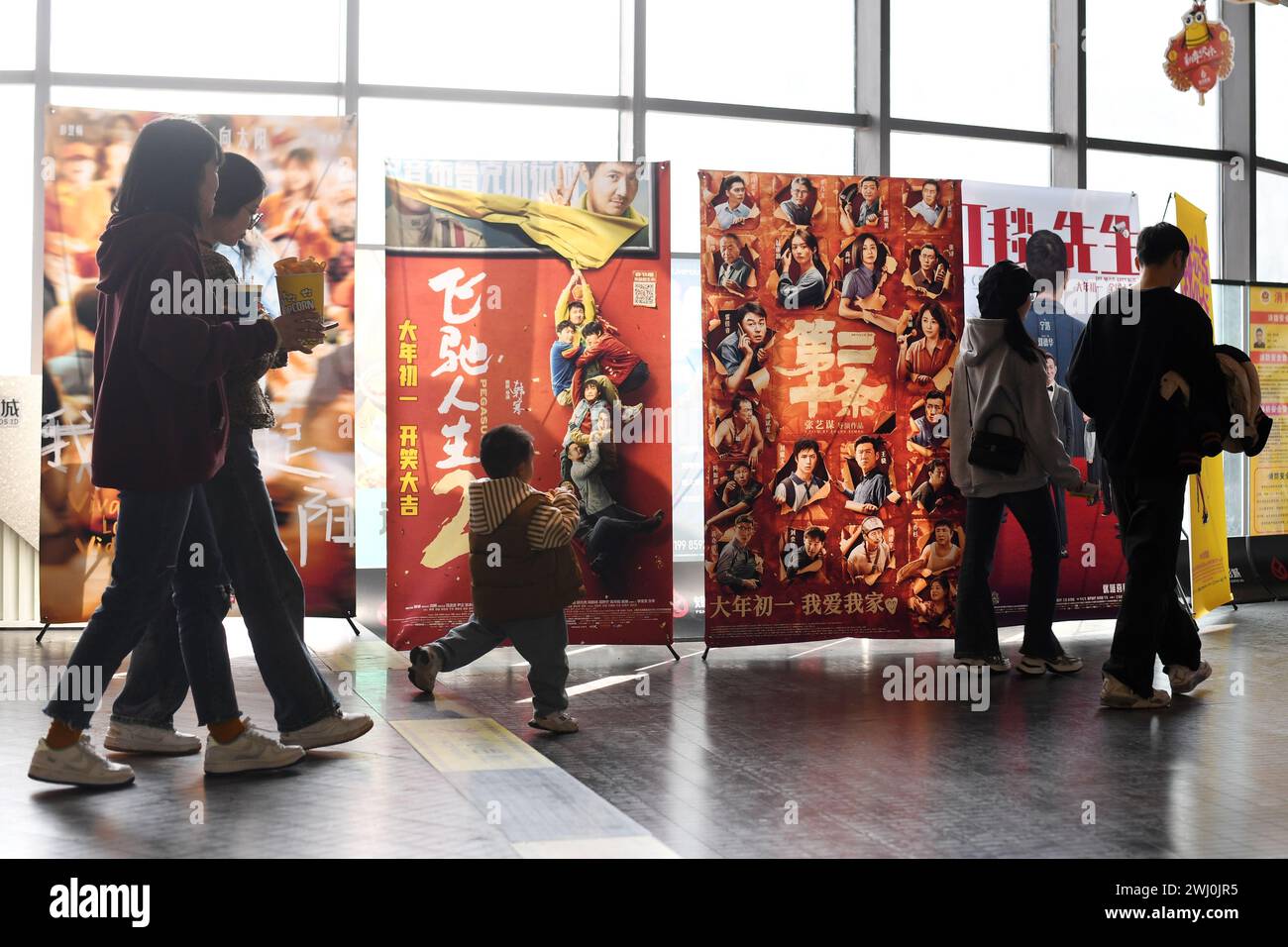 RENHUAI, CINA - 12 FEBBRAIO 2024 - le persone passano accanto ai poster dei film dell'anno lunare cinese al cinema Fenghe nella città di Renhuai, nel sud-ovest della Cina a Guizhou Foto Stock