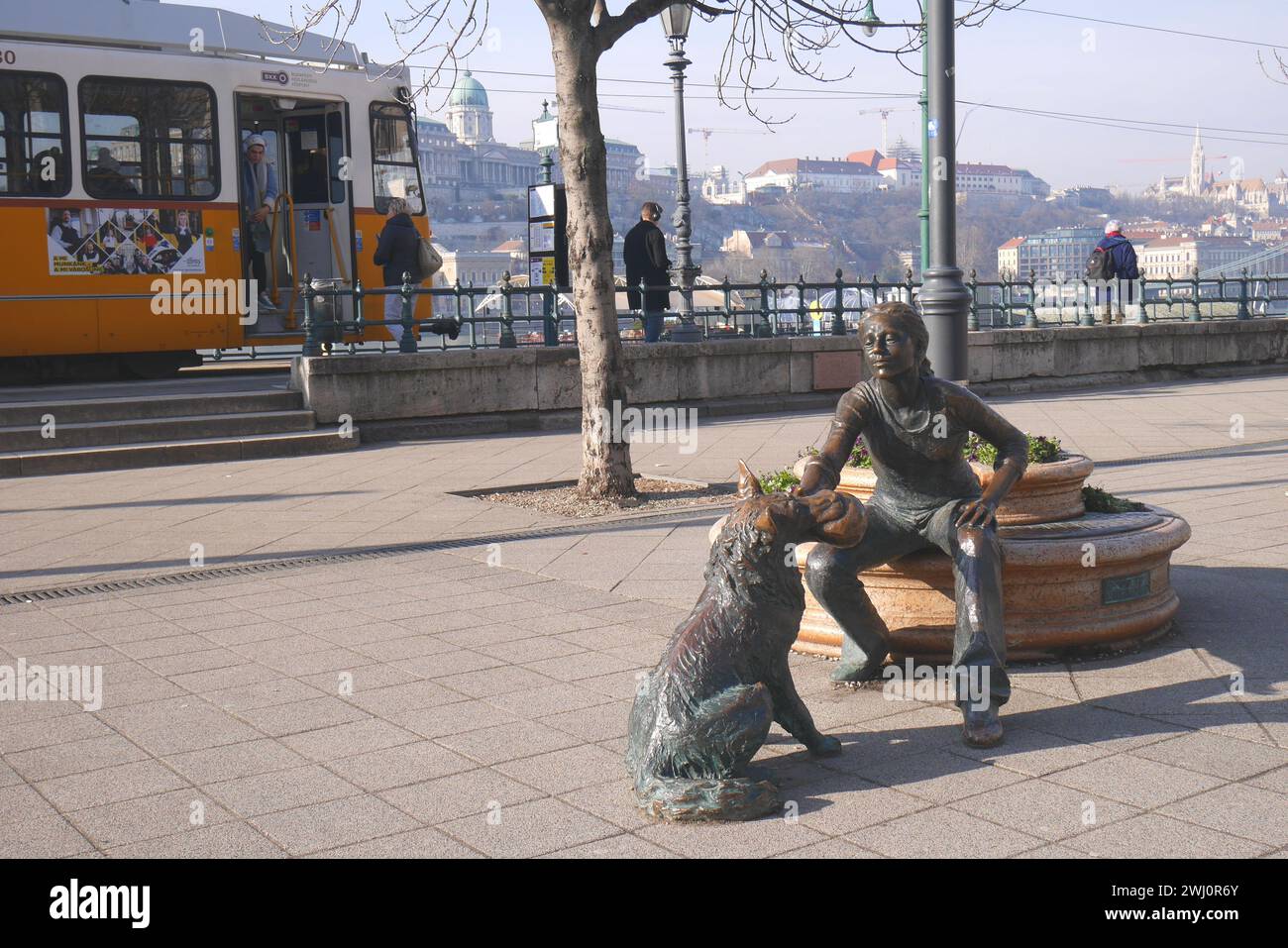 Statua di bronzo di una ragazza che gioca con un cane con un tram dietro, di Raffay Dávid, argine del Danubio, Pest, Budapest, Ungheria Foto Stock