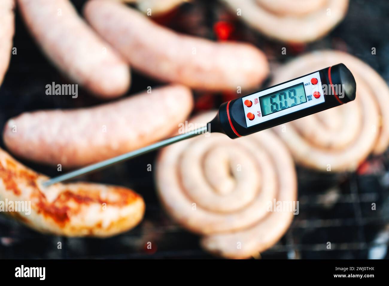 Primo piano di un termometro digitale per la carne che visualizza la temperatura al di sotto della soglia di cottura sicura per le salsicce grigliate, segnalando una potenziale guarigione Foto Stock