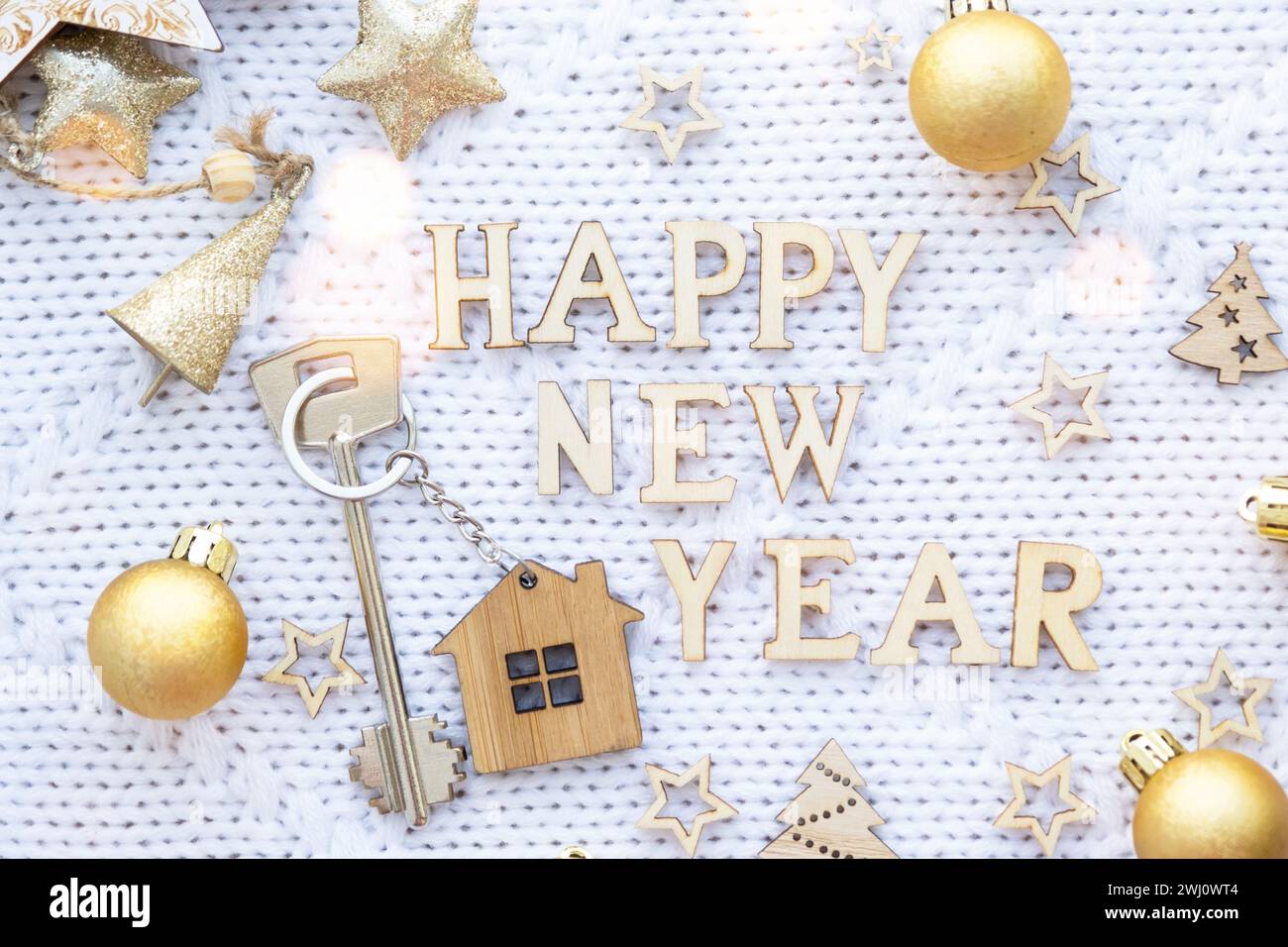 Chiave della casa con cottage portachiavi su sfondo natalizio a maglia con stelle, luci di ghirlande. Felice anno nuovo lettere di legno, gre Foto Stock