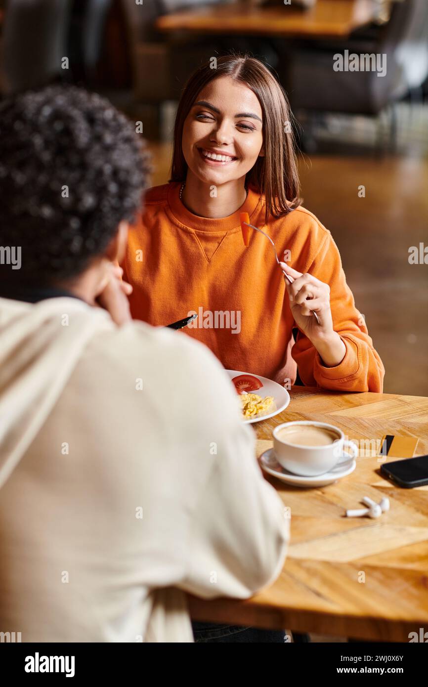 Sorridente giovane donna che ha una piacevole conversazione con il fidanzato durante un pasto in un accogliente caffè Foto Stock
