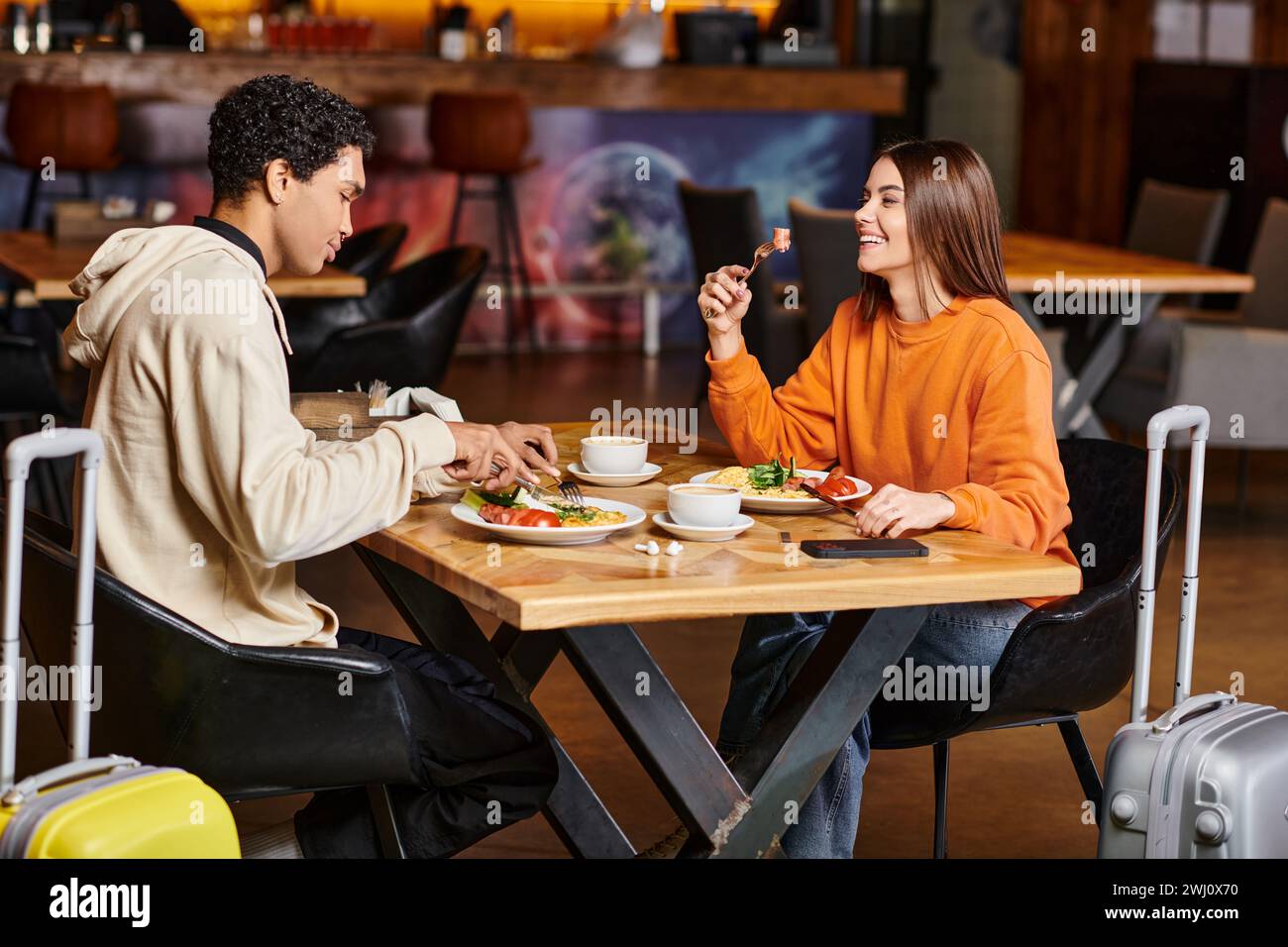 coppie diverse che condividono un momento di gioia con un pasto sano in un caffè alla moda, bagagli da viaggio Foto Stock