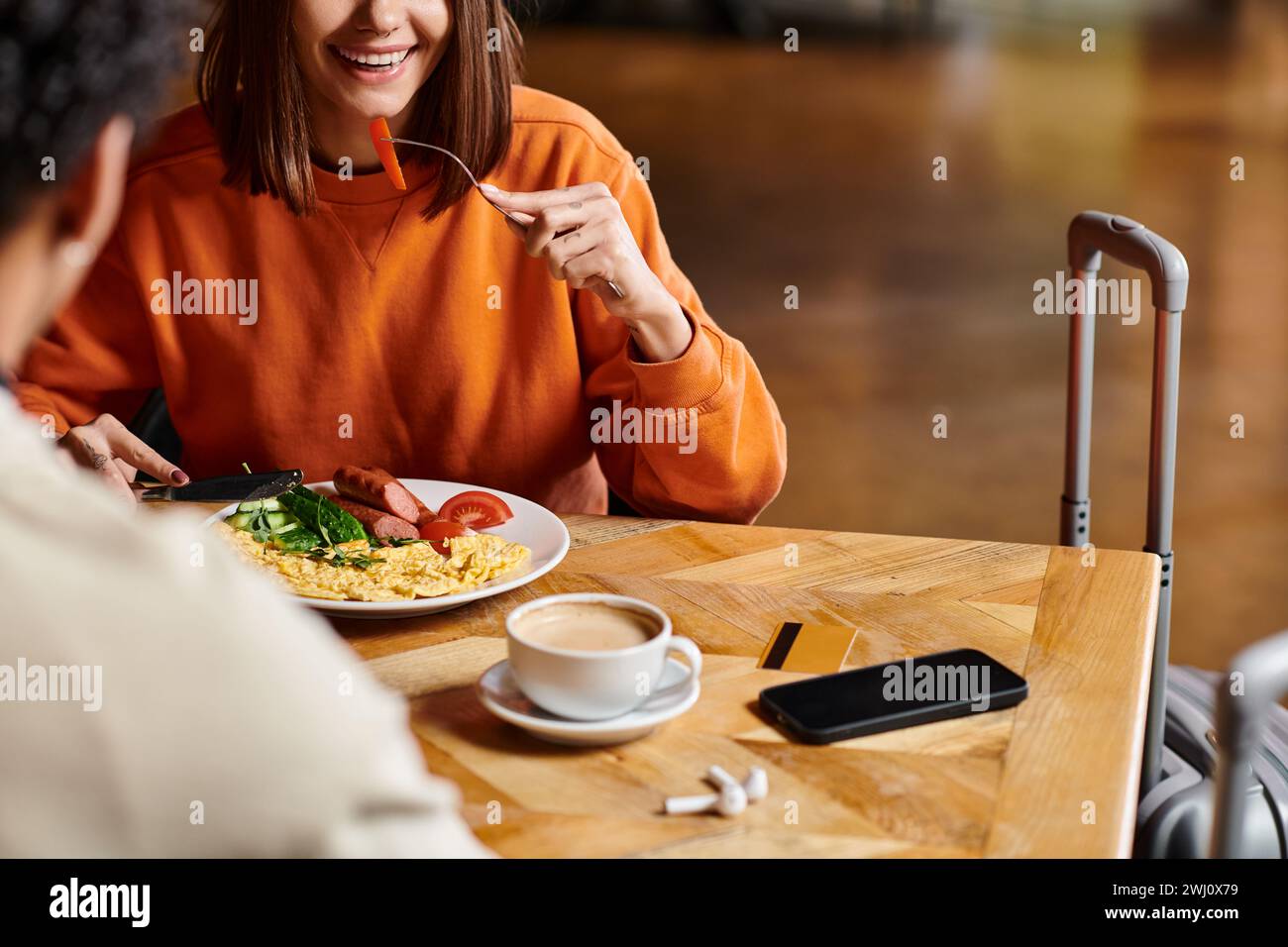 donna felice che fa colazione vicino a una tazza calda di caffè mentre si gode un pasto gustoso vicino al ragazzo nero Foto Stock