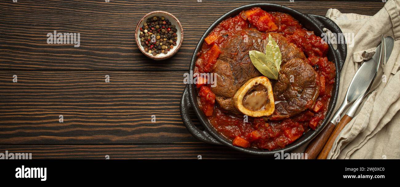 Piatto tradizionale italiano Ossobuco tutti milanesi a base di gambo di vitello tagliato con salsa di pomodoro vegetale servito in cassero nero Foto Stock