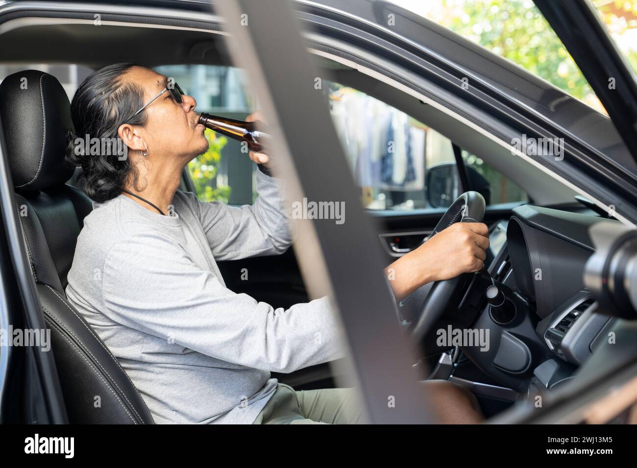 Un giovane asiatico ubriaco guida un'auto con una bottiglia di birra, un concetto di guida pericoloso. Foto Stock