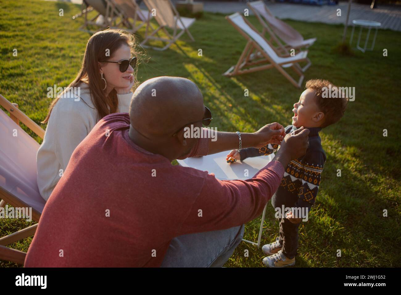 Famiglia multietnica con bambini che si divertono nel parco naturale. Papà afroamericano gioca con suo figlio al tramonto. Momento autentico, stile di vita. Foto Stock
