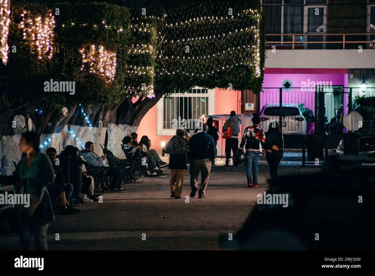 Gruppo di persone in piedi in un vicolo poco illuminato accanto ad un edificio adornato da luci natalizie Foto Stock