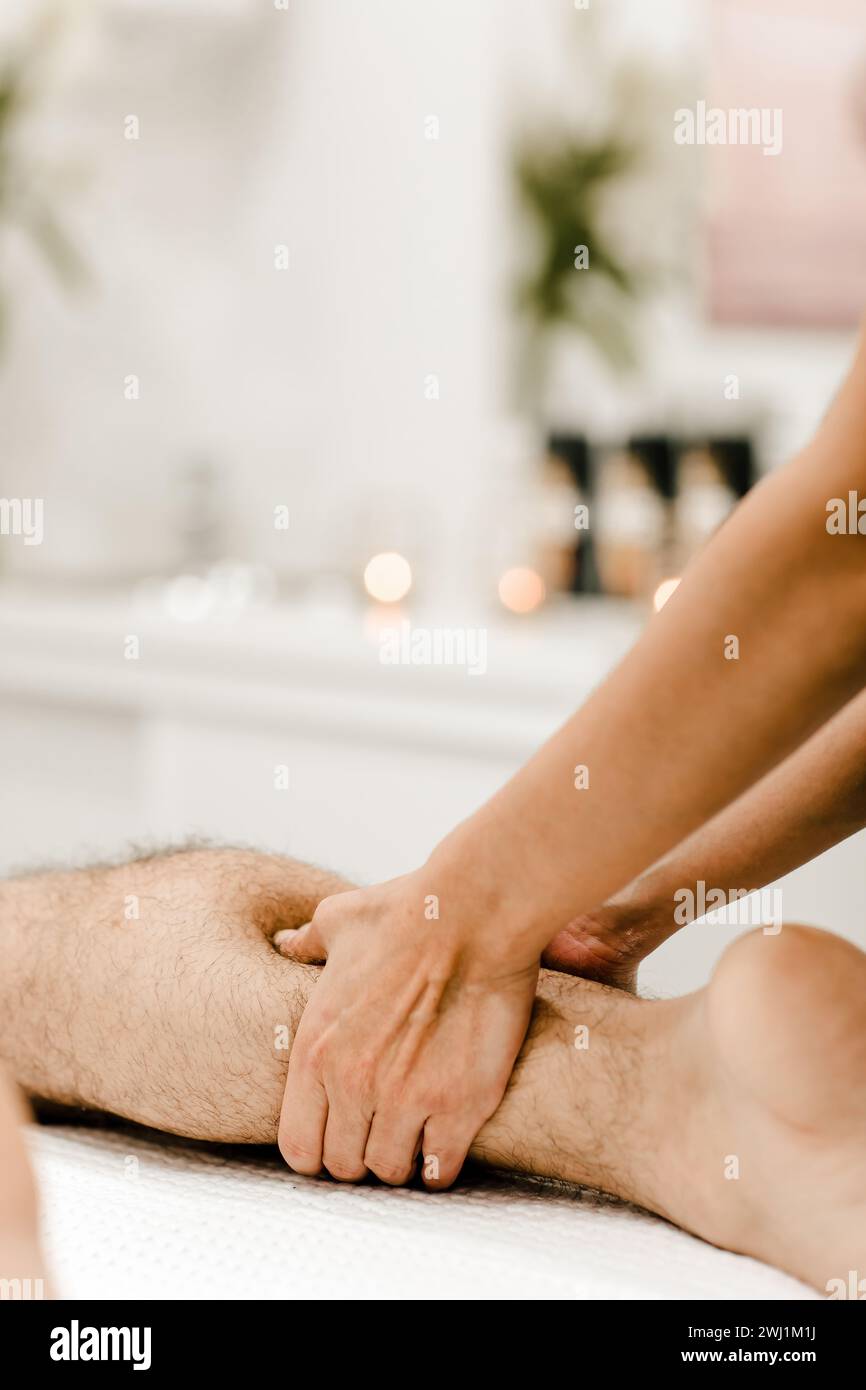Vista dettagliata di un massaggio alle gambe su un uomo, concentrandosi sul rilassamento muscolare e sulle tecniche terapeutiche. Foto Stock