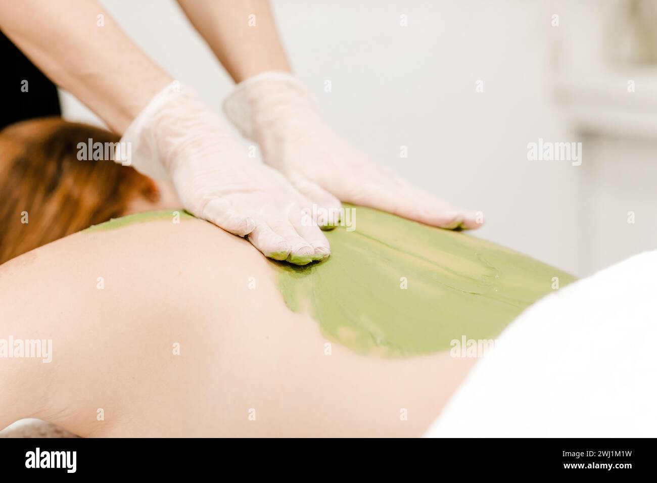 Donna che riceve un massaggio terapeutico alla schiena con alghe verdi, enfatizzando il relax e il trattamento naturale per la cura della pelle Foto Stock