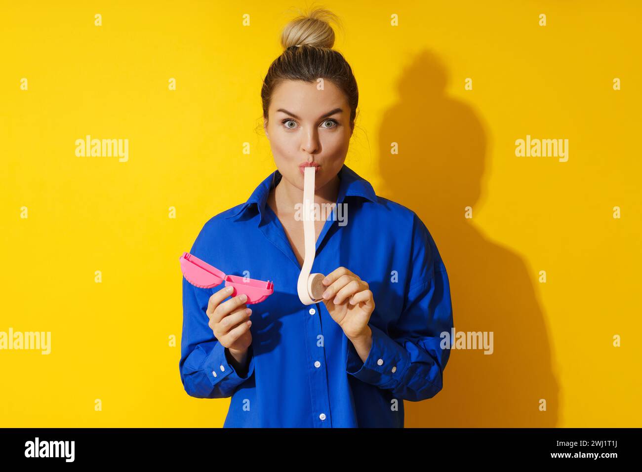 Giovane donna che assaggia gomma da masticare su sfondo giallo Foto Stock