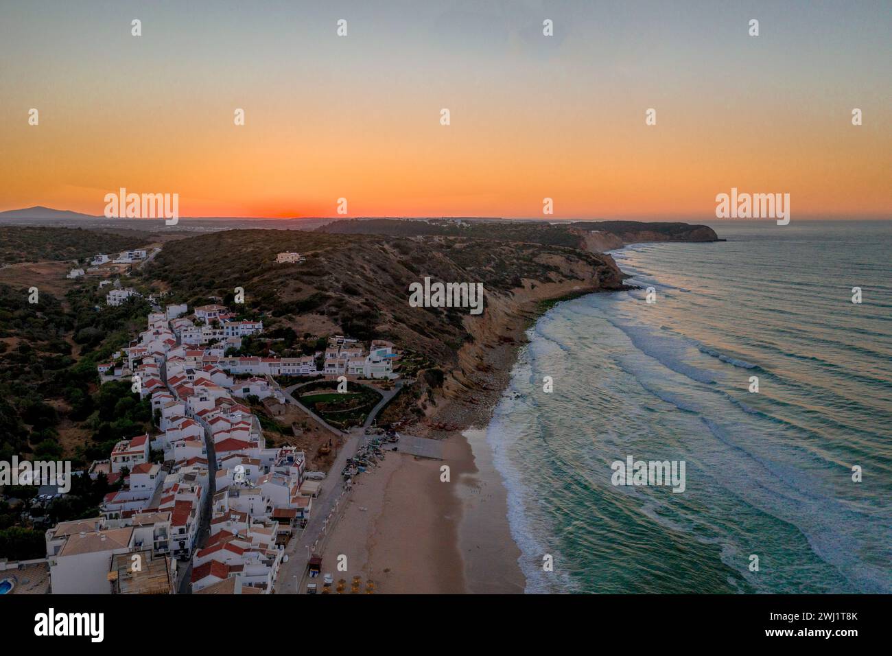 Una vista aerea del tramonto su una città costiera con onde che si infrangono Foto Stock