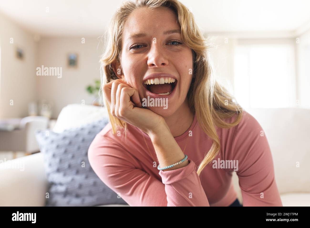 Felice bionda donna caucasica che sta videochiamando e ridendo nel soleggiato soggiorno Foto Stock