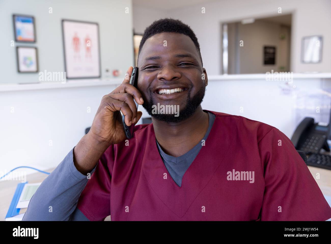 Ritratto di felice medico afroamericano maschio che parla su smartphone nella reception dell'ospedale Foto Stock