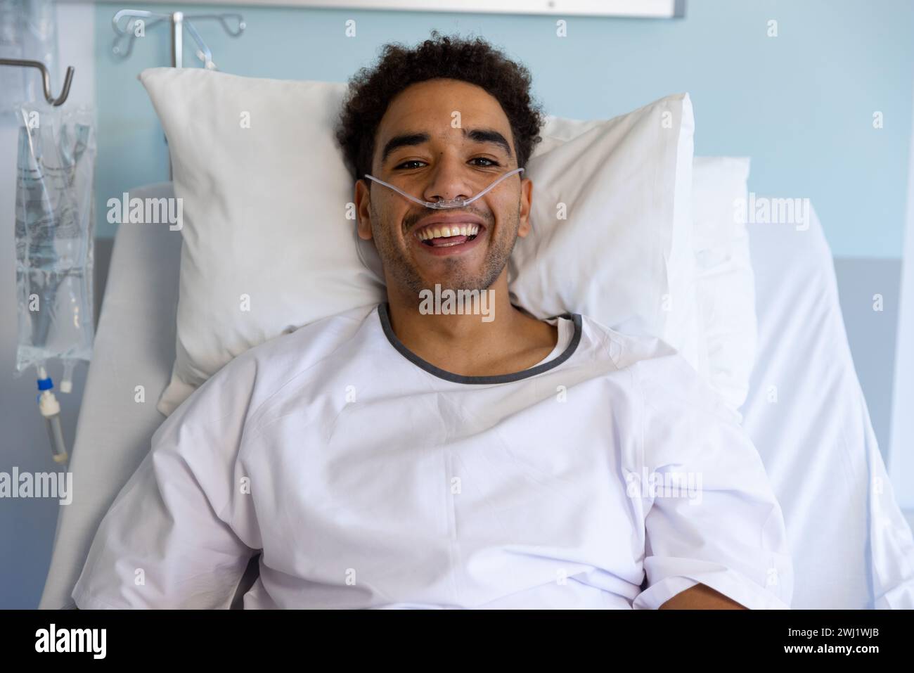 Ritratto di felice paziente maschio birazziale a letto in soleggiata stanza d'ospedale Foto Stock