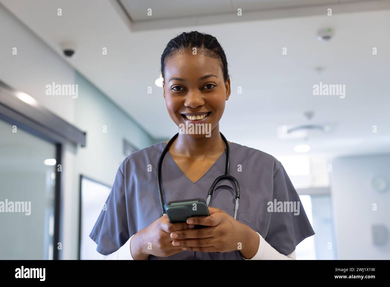Ritratto di felice afroamericana medico utilizzando smartphone in corridoio ospedale Foto Stock