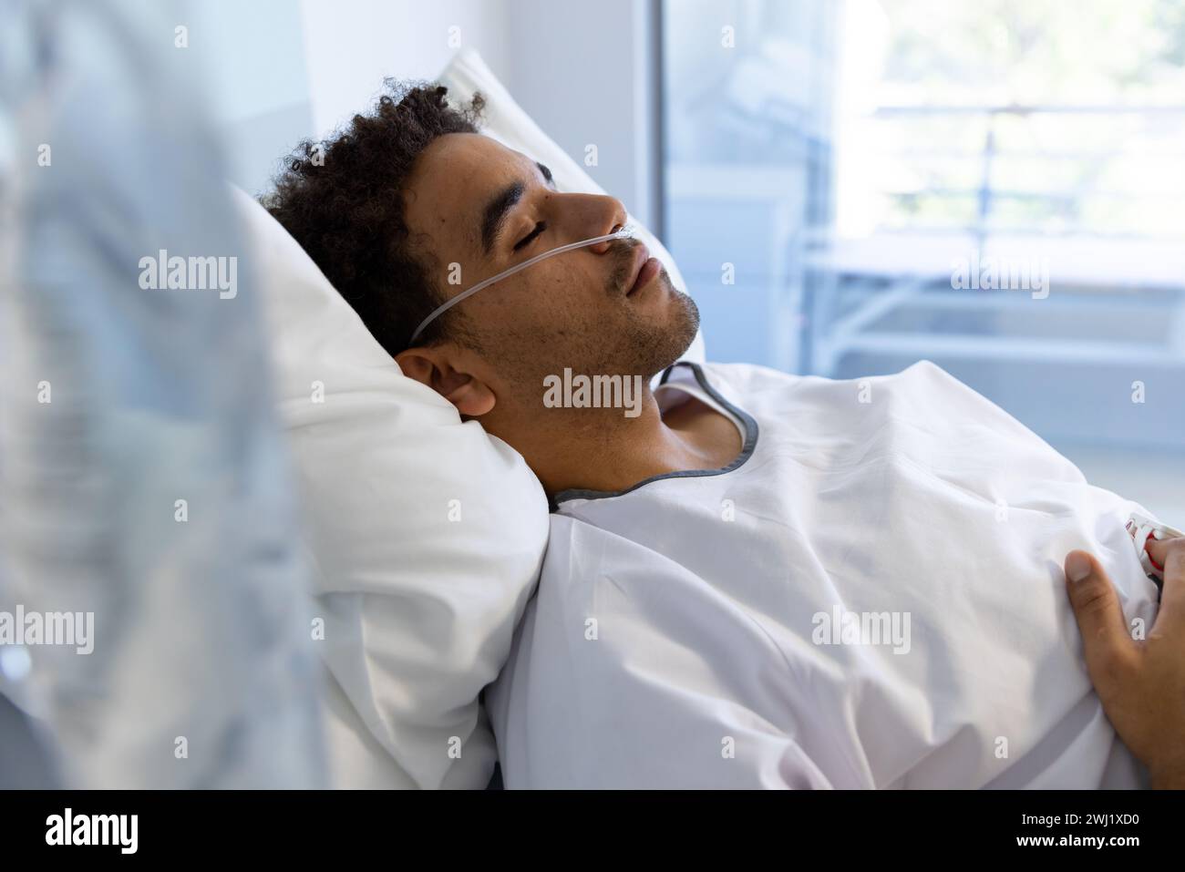 Paziente maschio birazziale che dorme nel letto in soleggiata stanza d'ospedale Foto Stock