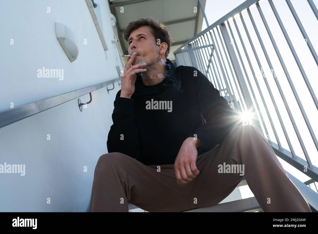 Uomo adulto che fuma sigaretta RYO o cannabis su una scala accanto a casa sua Foto Stock