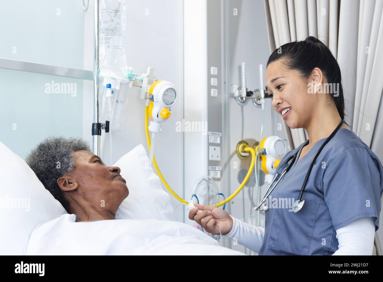 Medico femminile diversificato che parla con una paziente anziana in camera d'ospedale Foto Stock