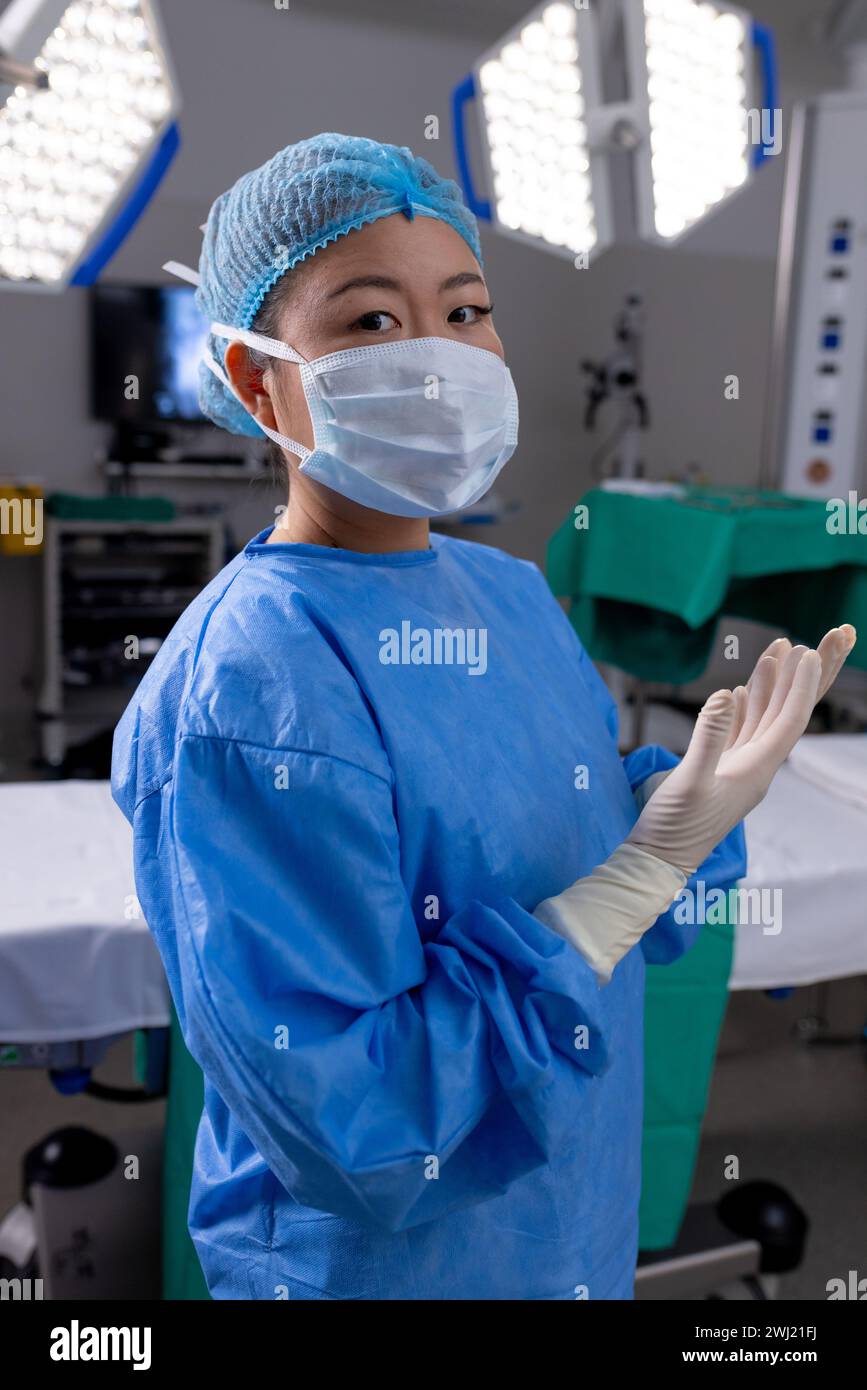 Ritratto di medico femminile asiatico con maschera facciale e guanti in sala operatoria dell'ospedale Foto Stock