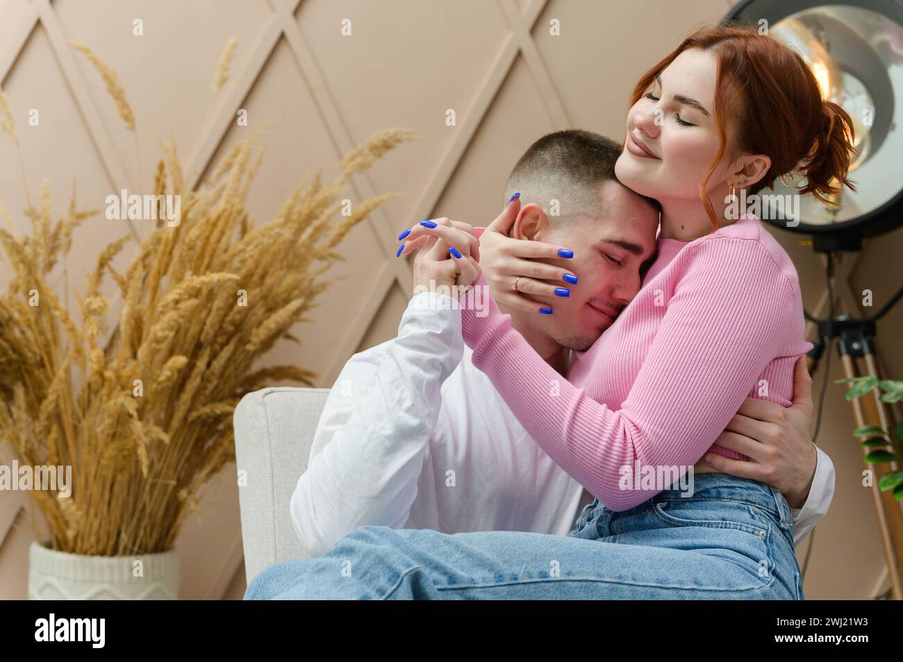 Una giovane coppia romantica si abbraccia mentre si siede su una sedia. Una ragazza si siede in grembo di un uomo. La ragazza spinge la testa dell'uomo sul petto. Foto Stock