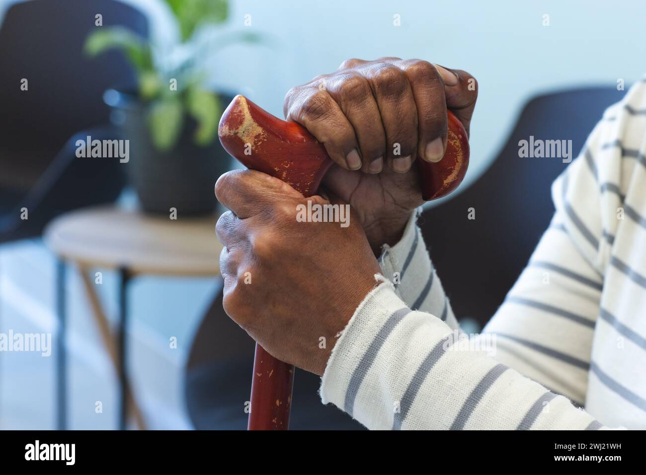Mani di donna anziana afroamericana con bastone da passeggio seduto nella sala d'attesa dell'ospedale Foto Stock
