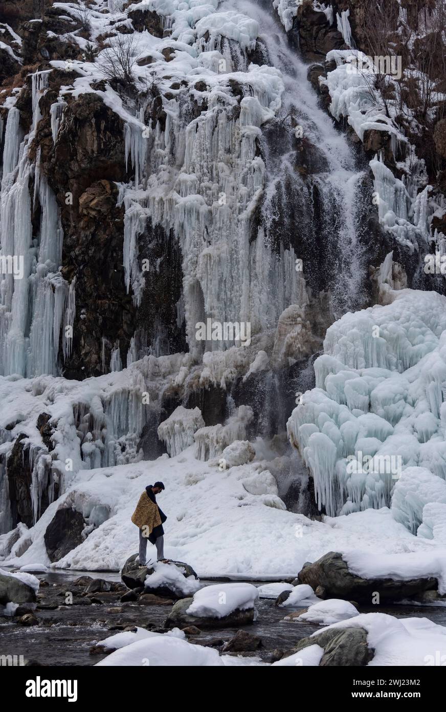 Baramulla, India. 12 febbraio 2024. Un uomo sta su una roccia di fronte a una cascata parzialmente congelata durante una giornata di sole. Dopo un lungo inverno secco e caldo, la valle ha visto abbondanti nevicate e piogge la scorsa settimana. La valle è attualmente nella fase moderata dell'inverno, Chillai Khurd, dopo la fine del periodo più duro di 40 giorni il 30 gennaio. Credito: SOPA Images Limited/Alamy Live News Foto Stock