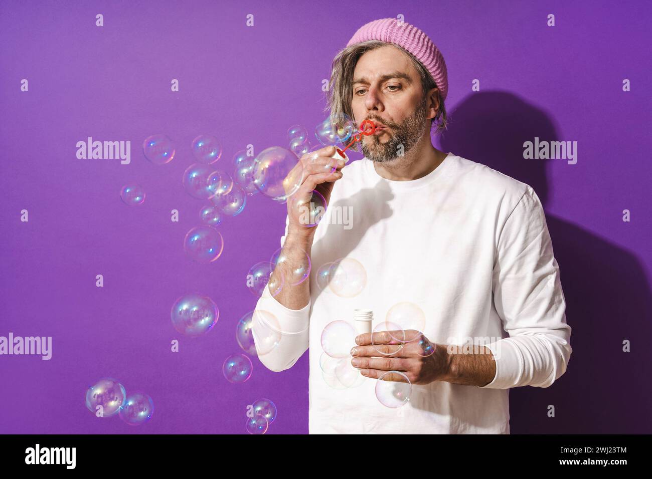 Uomo di mezza età spensierato che soffia bolle di sapone su sfondo viola Foto Stock