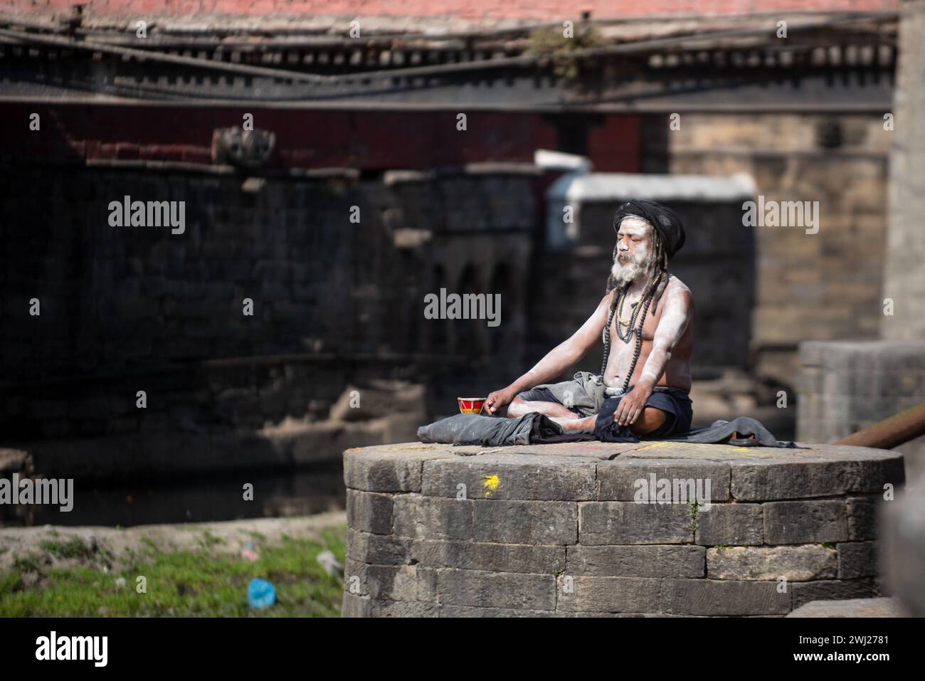 Un sadhu o un sacerdote indù con abito nero noto come Aghori meditano al tempio di Pashupatinath sulla riva del sacro luogo crematorio del fiume Bagmati, Kathmandu, Nepal, lunedì 12 febbraio 2024 Foto Stock