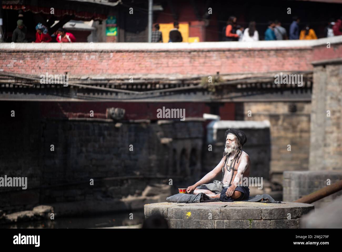 Un sadhu o un sacerdote indù con abito nero noto come Aghori meditano al tempio di Pashupatinath sulla riva del sacro luogo crematorio del fiume Bagmati, Kathmandu, Nepal, lunedì 12 febbraio 2024 Foto Stock