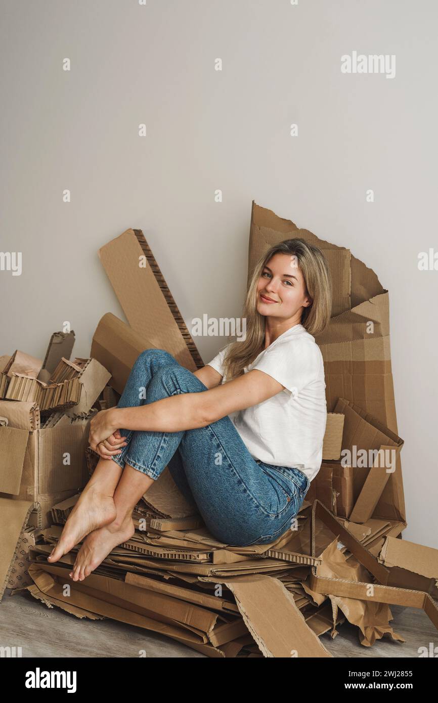 Una giovane donna con bacchetta di rifiuti di cartone a casa. Concetti di riciclaggio della carta e smistamento dei rifiuti Foto Stock