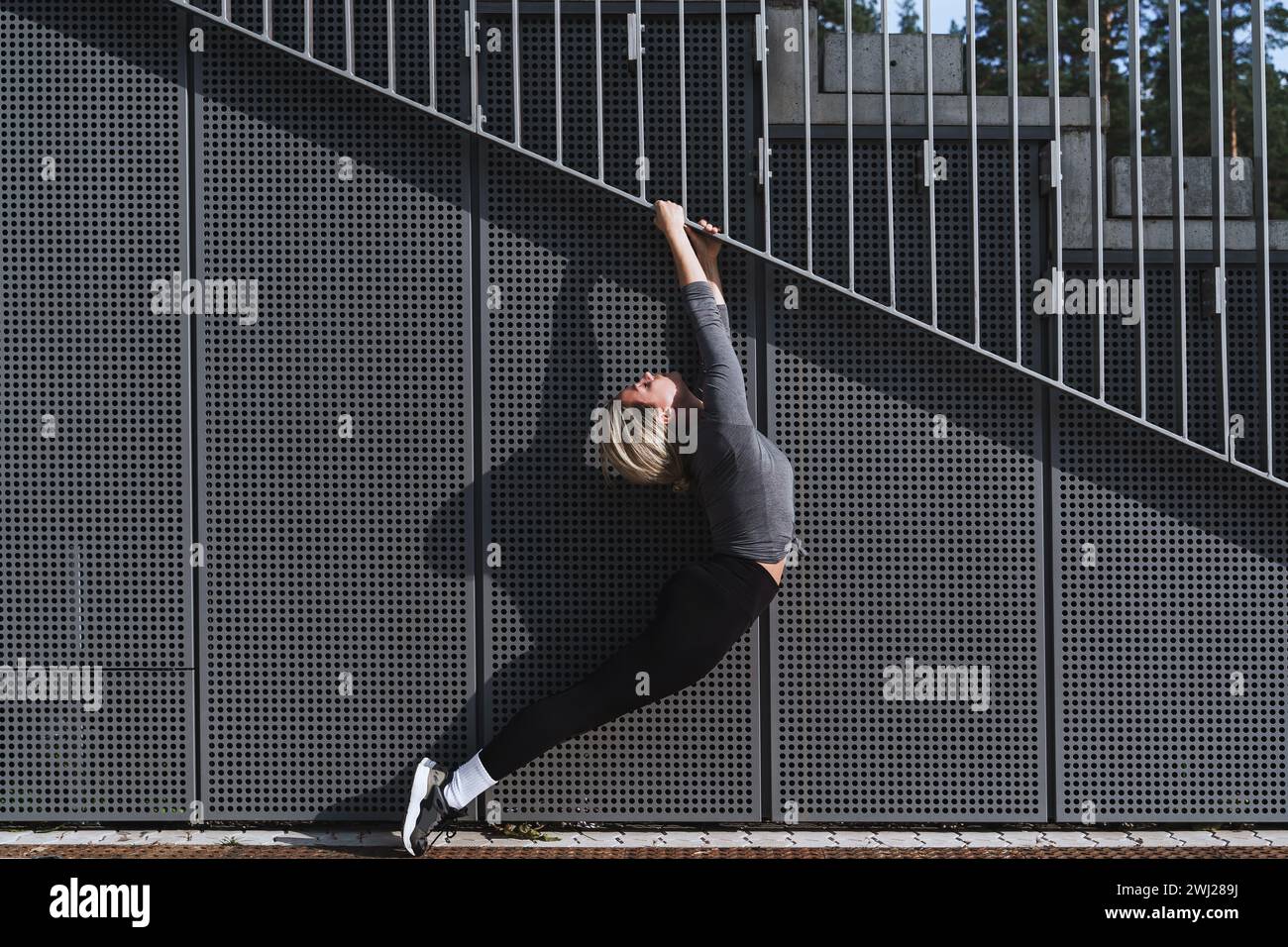 Atleta donna che indossa abbigliamento sportivo femminile che si allunga sullo sfondo moderno con pannelli in acciaio Foto Stock