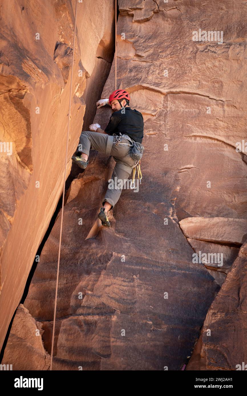 Vista ad angolo basso dell'uomo determinato che sale dalla scogliera rocciosa Foto Stock