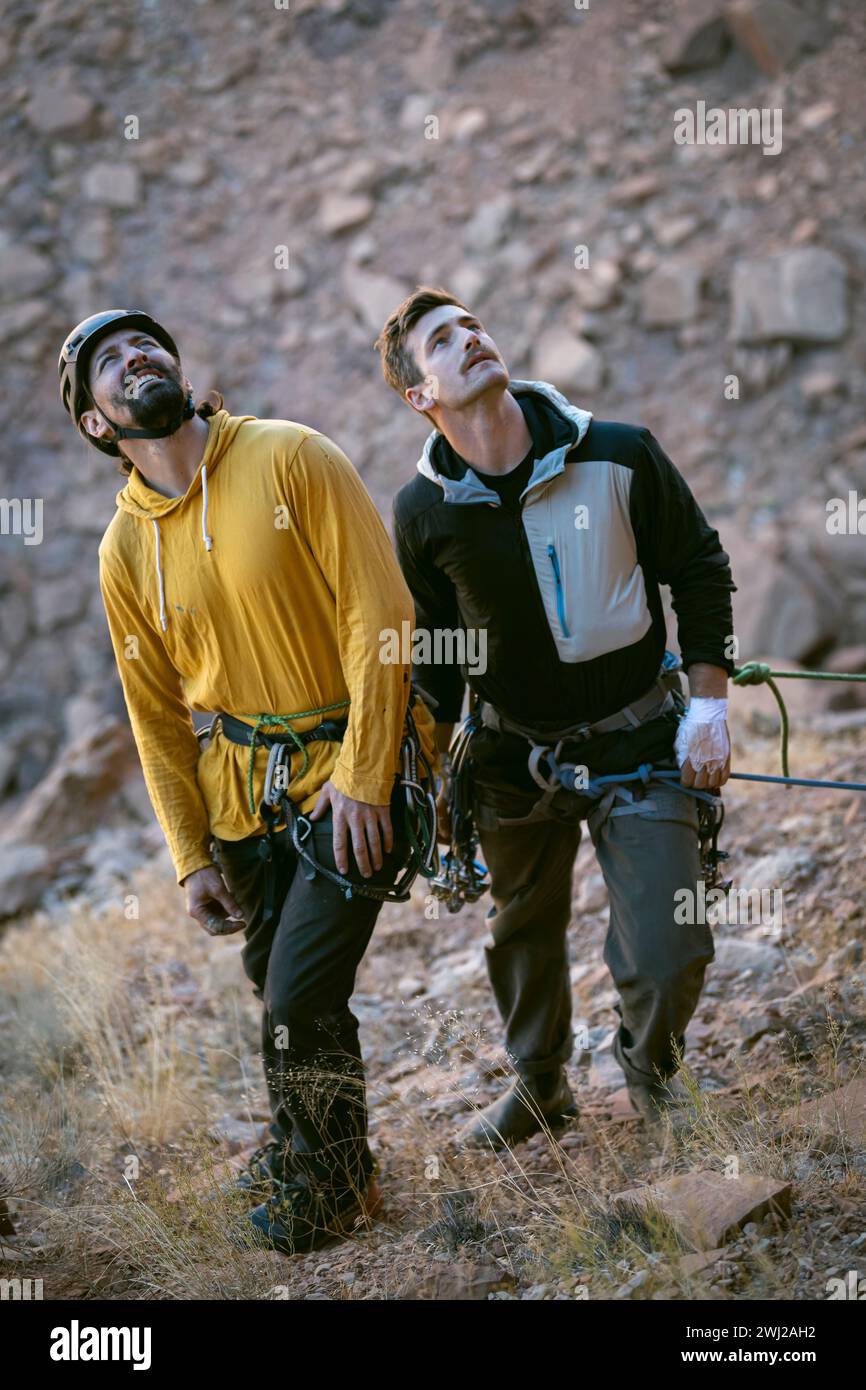 Uomini con attrezzatura da arrampicata che guardano in alto mentre si alzano in piedi sulla montagna Foto Stock