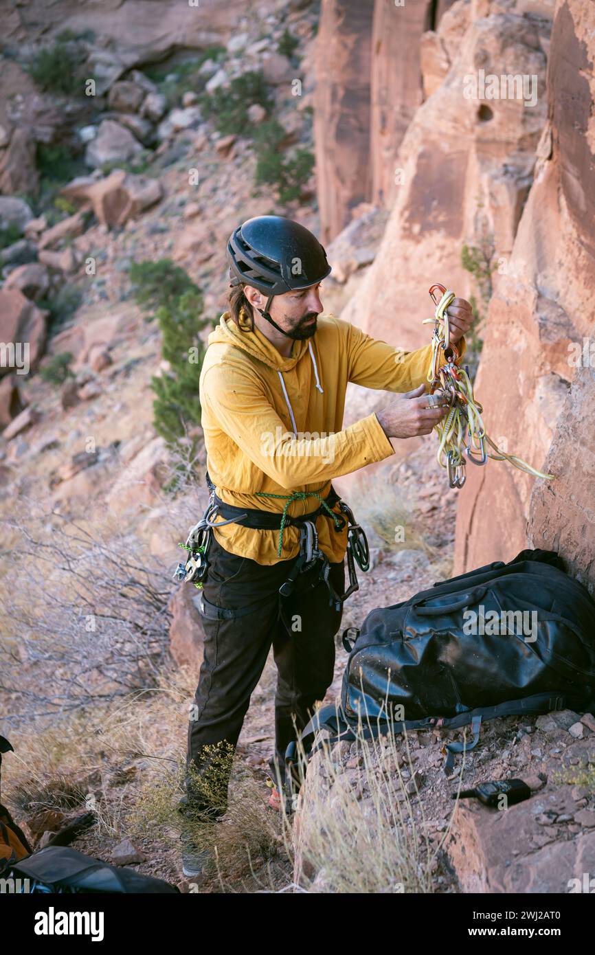 Alpinista maschio che tiene in mano i moschettoni mentre si trova sulla scogliera nel deserto Foto Stock