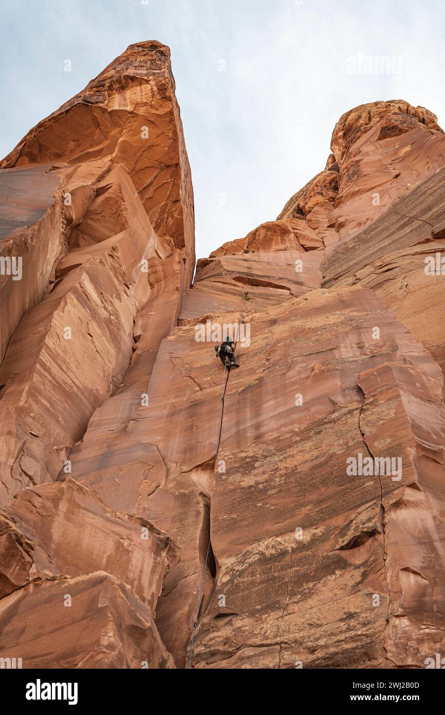 Vista ad angolo basso di un determinato alpinista che sale su un'alta scogliera rocciosa Foto Stock