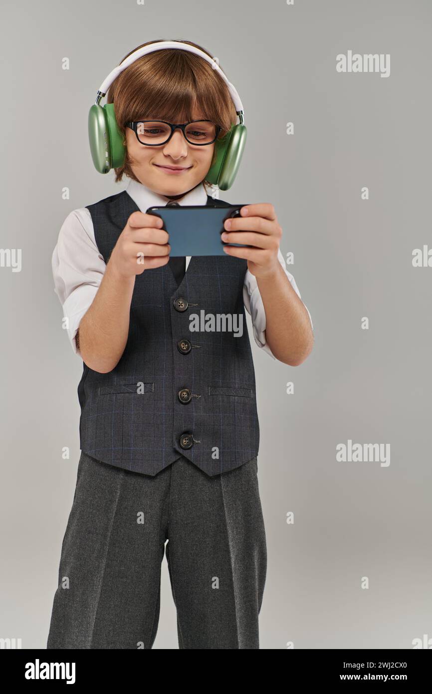 elegante ragazzo con occhiali e abbigliamento elegante che ascolta la musica con le cuffie e gioca con il cellulare Foto Stock