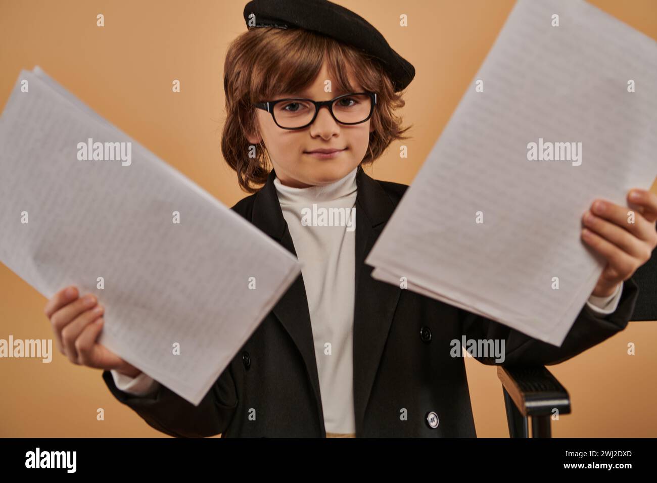 il ragazzo, vestito con abiti eleganti e con occhiali, si regge con sicurezza con la carta in mano Foto Stock