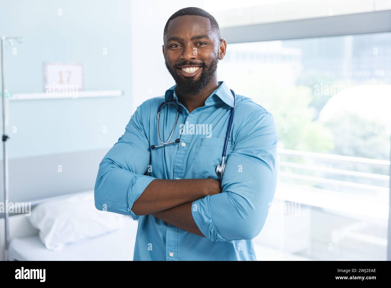 Ritratto del medico maschio afro-americano felice che indossa camicia blu e stetoscopio in camera d'ospedale Foto Stock
