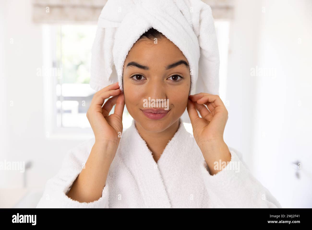 Ritratto di donna birazziale in accappatoio e con un asciugamano sulla testa nel bagno soleggiato Foto Stock