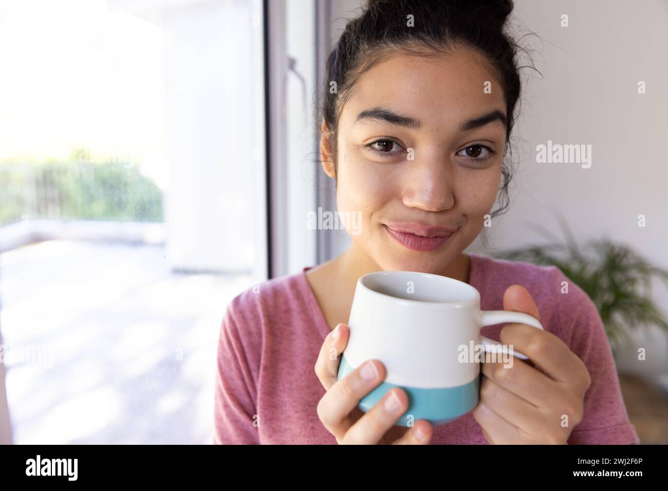 Felice donna birazziale che tiene una tazza di caffè in una casa soleggiata Foto Stock