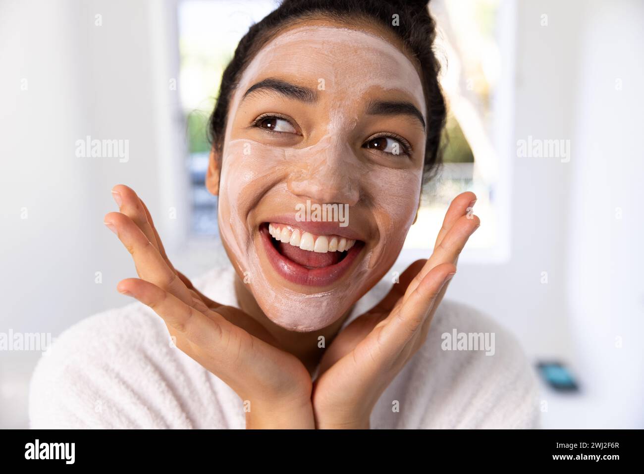 Ritratto di felice donna birazziale in accappatoio con maschera in bagno soleggiato Foto Stock