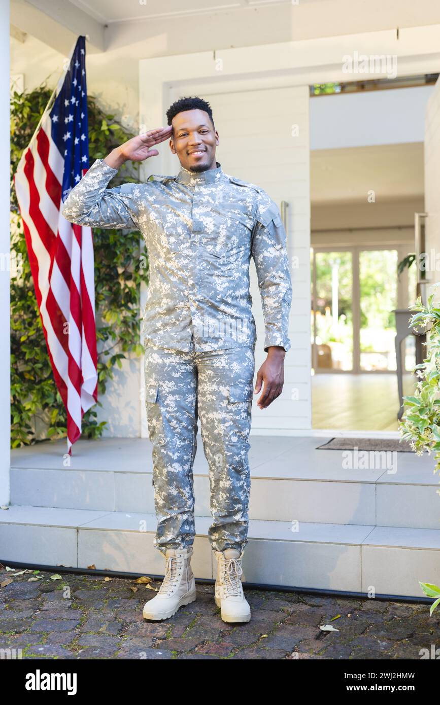 Felice soldato afroamericano in piedi e salutando fuori casa con la bandiera degli stati uniti, spazio copia Foto Stock