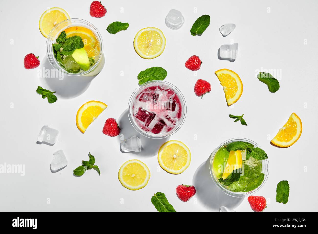 Tre bicchieri con limonate e cubetti di ghiaccio, limoni, fragole e foglie di menta su sfondo bianco. Vista dall'alto Foto Stock