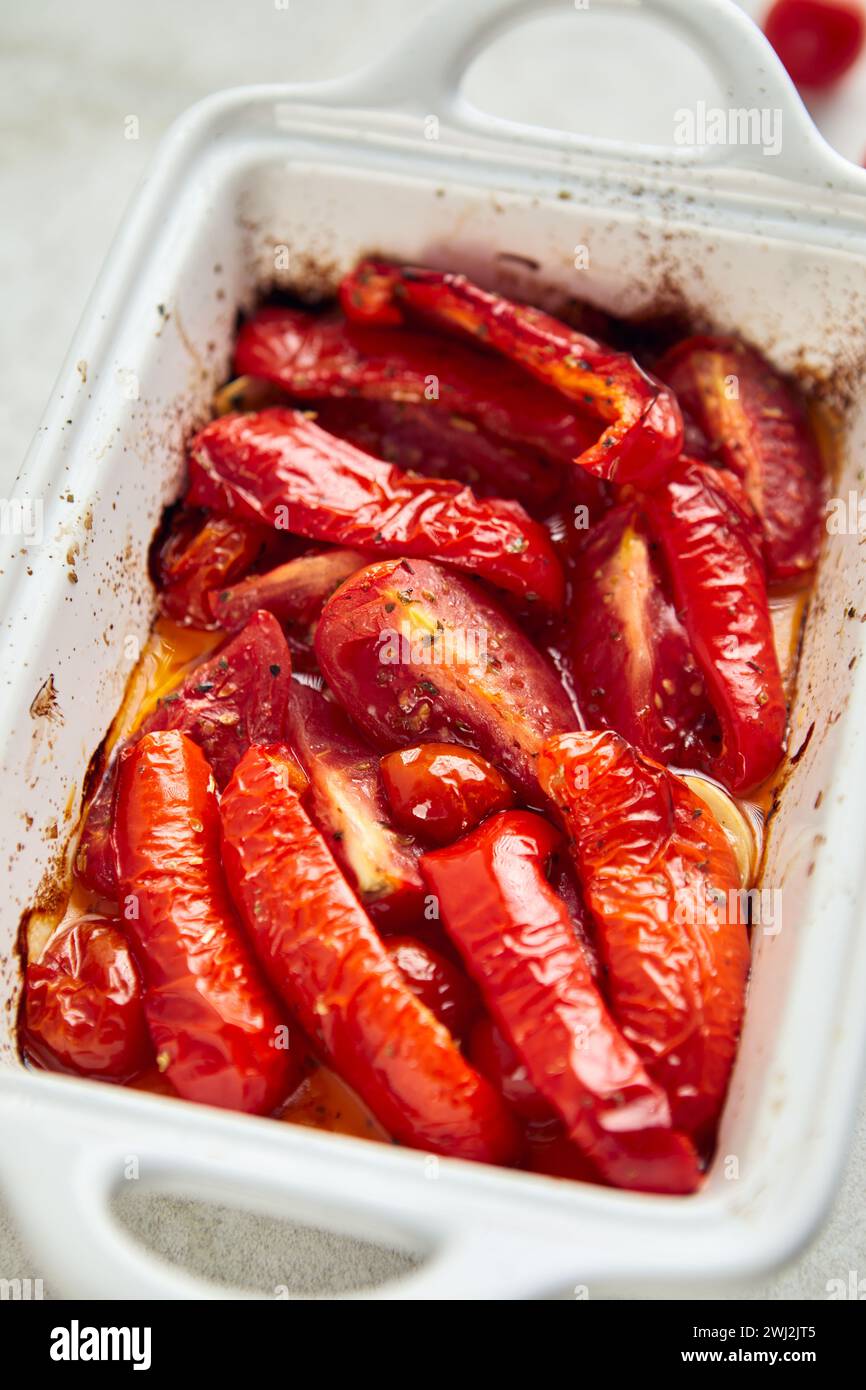 Pomodori e peperoni al forno con aglio ed erbe aromatiche in ceramica Foto Stock